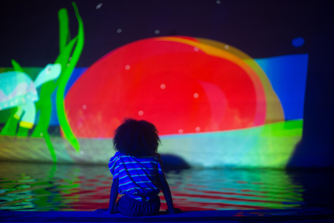 Kid sitting by the lake and watching the projections over a surface.